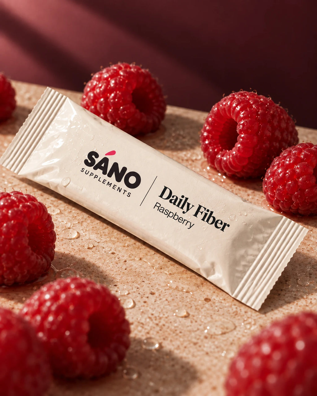 A single Sáno Daily Fiber sachet in raspberry among fresh raspberries