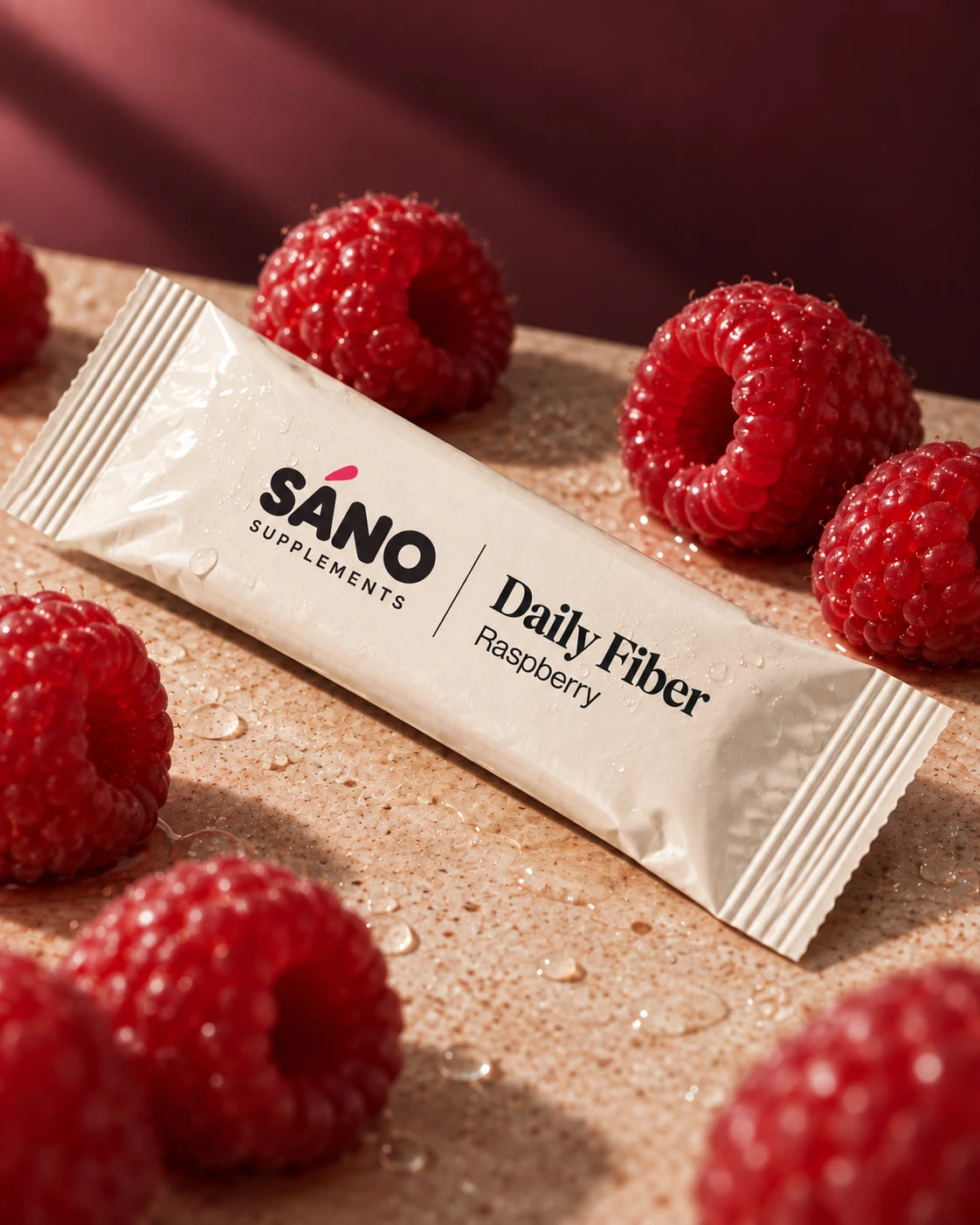 A single Sáno Daily Fiber sachet in raspberry among fresh raspberries