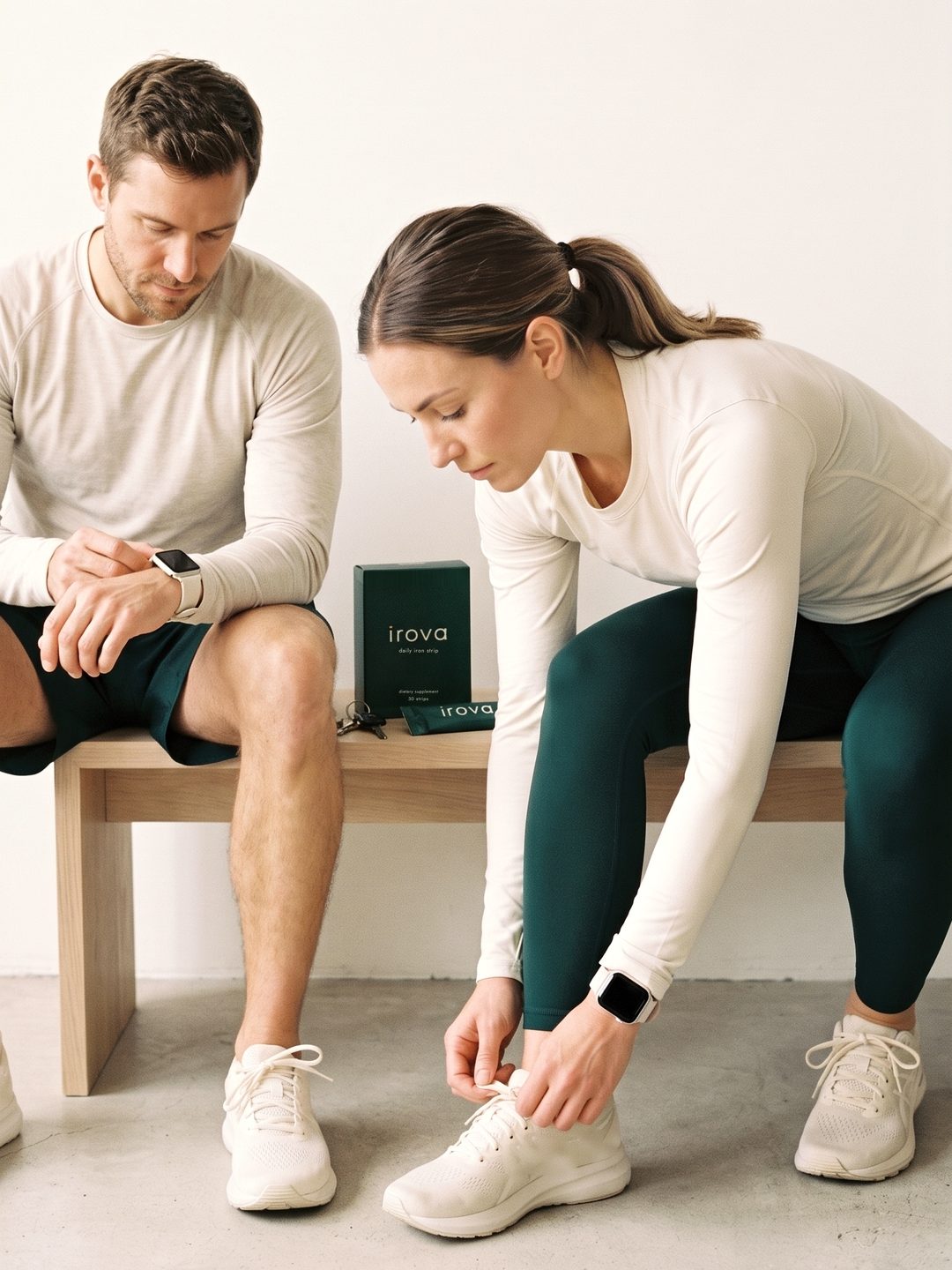 A man and a woman on a wooden bench getting ready for a run, with an Irova box and sachet between them